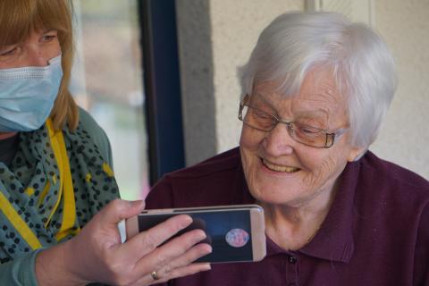 elder woman looking at a smartphone held by woman wearing mask