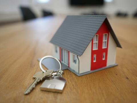 House key with a keychain next to a model of a house on a wooden table