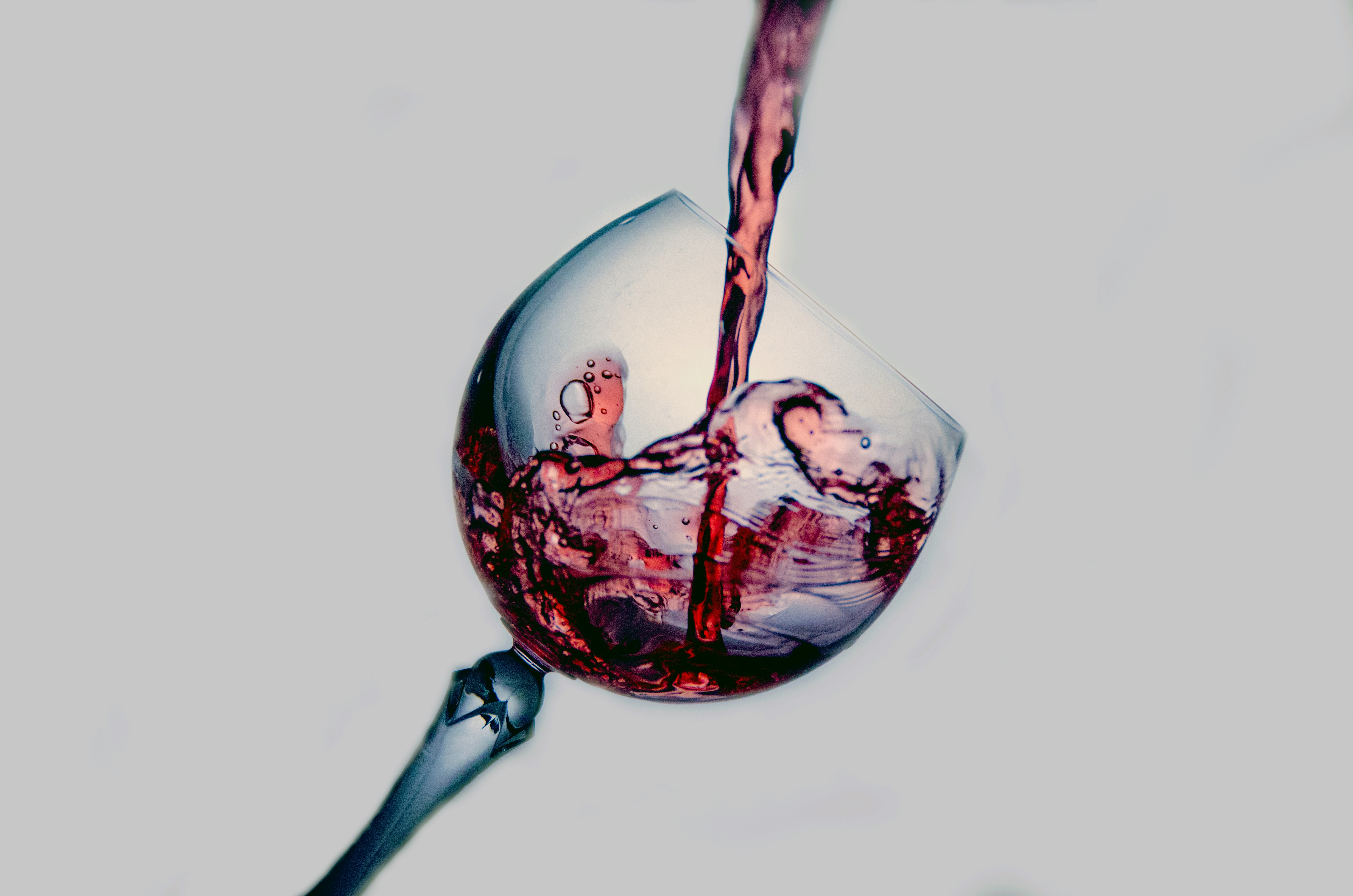Wine glass tilted on angle; red wine pours into the glass from above.